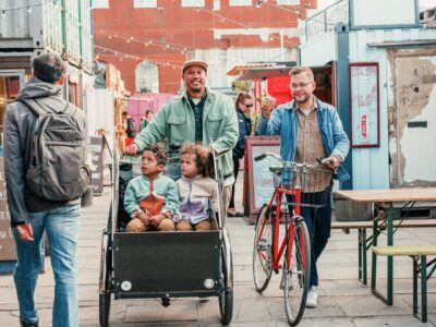 En man drar sina barn i en cykelvagn och en annan man går bredvid och leder sin cykel.