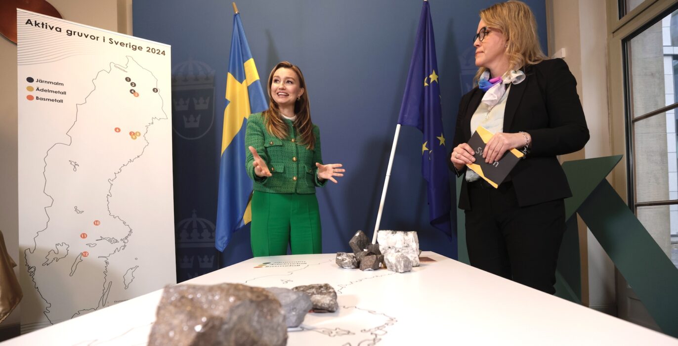 Ebba Busch med entusiastisk uppsyn i ett rum med olika Sverigekartor, stenar och svenska flaggan i bakgrunden. Emma Härdmark, kommunikationschef SveMin syns också i bild.
