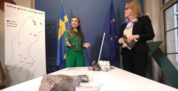 Ebba Busch med entusiastisk uppsyn i ett rum med olika Sverigekartor, stenar och svenska flaggan i bakgrunden. Emma Härdmark, kommunikationschef SveMin syns också i bild.