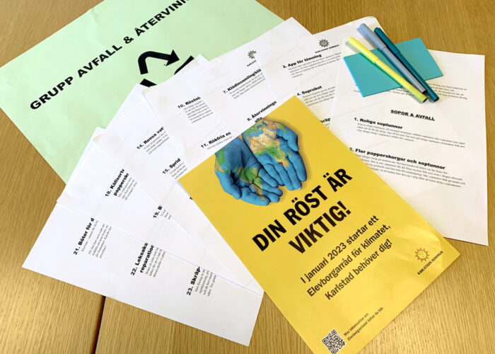 Workshopmaterial i en hög, överst en flyer med texten Din röst är viktig och två händer målade som en karta över jorden.