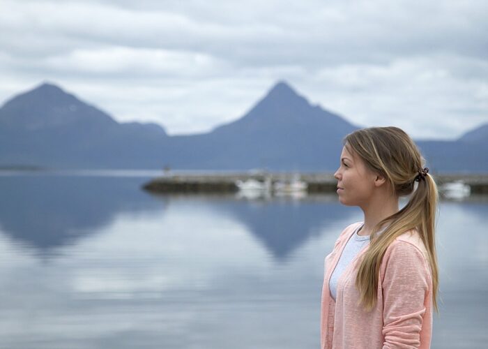 Blond kvinna i profil med en sjö och berg i bakgrunden.