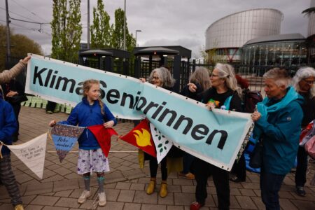 Barn står framför banderoll som hålls av äldre kvinnor.