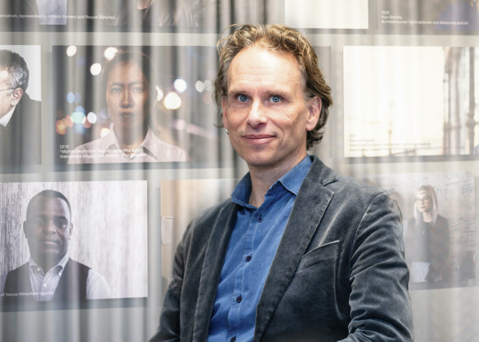 Porträtt av John Stauffer som tittar in i kameran, framför ett tunt draperi och med foton i bakgrunden.