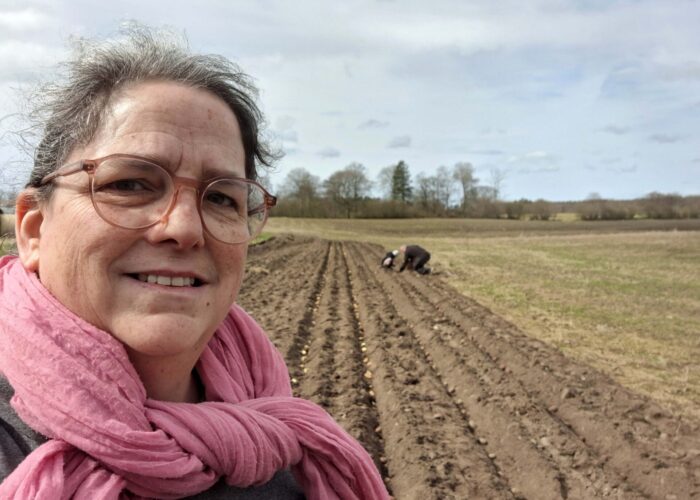 Kvinna med rosa sjal står framför mark där potatis just sätts.