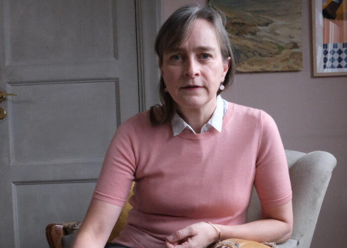 Porträtt av Nina Wormbs, rosaklädd i en sliten grå fåtölj.