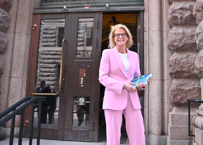 Elisabeth Svantesson i rosa kostym, leende utanför en port, med vårändringsbudgeten i händerna.
