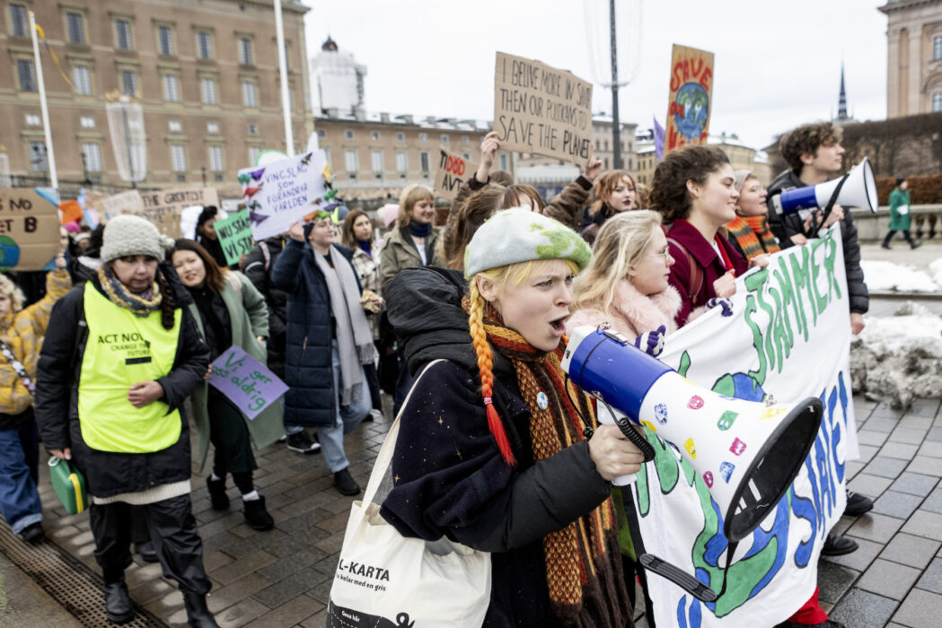 Klimataktivister med plakatet "Nu stämmer vi staten" demonstrerar framför slottet i Stockholm.