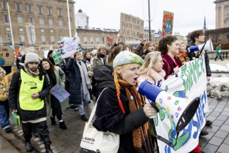 Klimataktivister med plakatet "Nu stämmer vi staten" demonstrerar framför slottet i Stockholm.