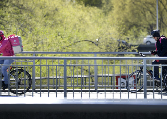 Två cykelbud på en bro, i bakgrunden gröna trädkronor.