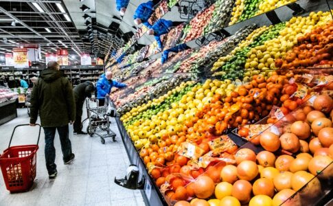 Kunder vid en frukt- och grönthylla i en stor matbutik.