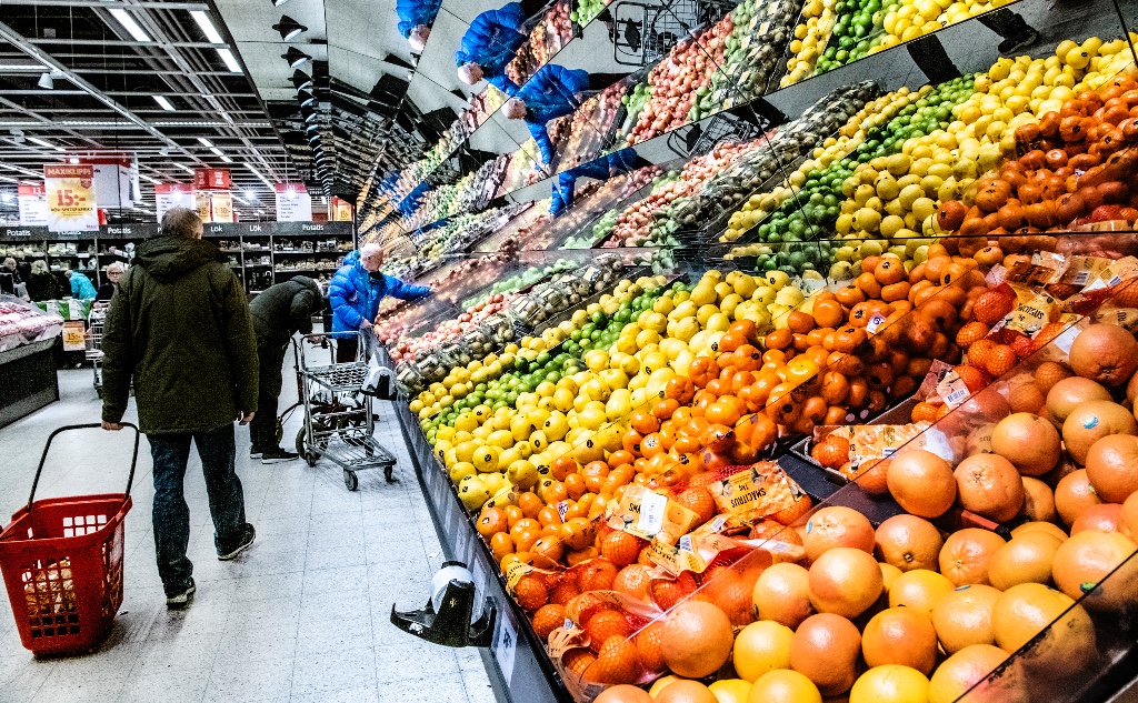Kunder vid en frukt- och grönthylla i en stor matbutik.
